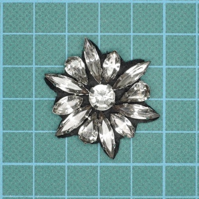 Broche floral com pedras transparentes sobre base quadriculada azul