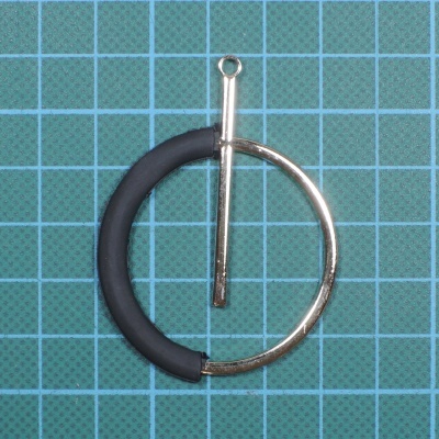 Brinco circular metálico dourado e preto sobre superfície quadriculada verde e azul