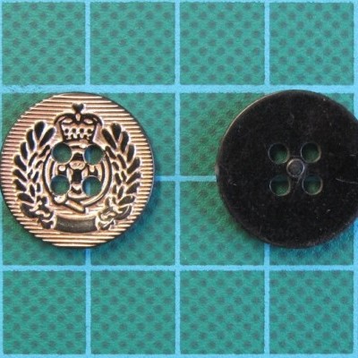 Dois botões, um dourado com coroa e outro preto liso, sobre superfície quadriculada verde