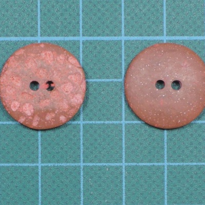 Dois botões castanhos, um texturizado e outro liso, sobre fundo quadriculado azul e verde.