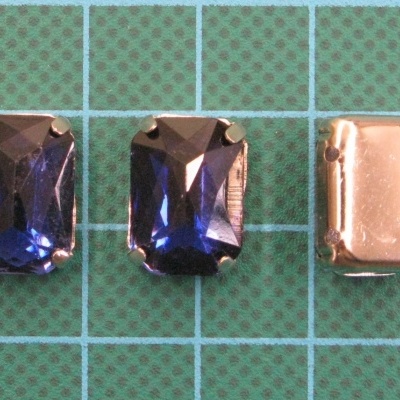 Três objetos retangulares com pedras azuis e metal sobre fundo verde quadriculado