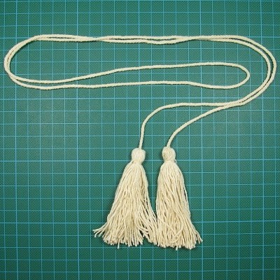 Cordão branco com duas borlas sobre superfície verde quadriculada