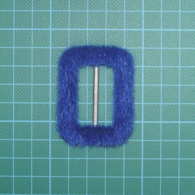 Fivela retangular azul felpuda com barra metálica sobre superfície de corte verde com grelha