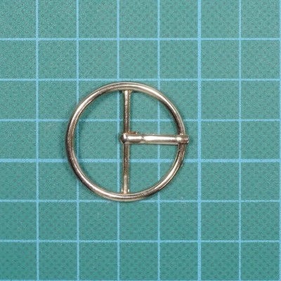 Fivela redonda metálica dourada sobre superfície verde com grade