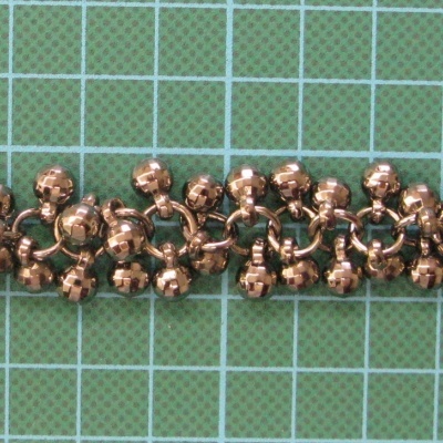 pulseira de metal bronze/cobre sobre fundo verde com grade