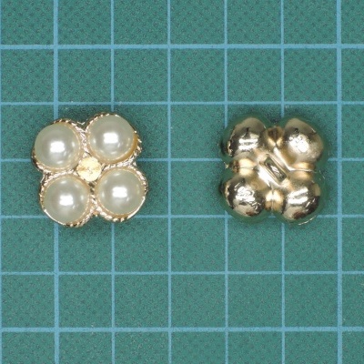 Botões metálicos dourados com pérolas falsas em forma de flor sobre fundo verde quadriculado