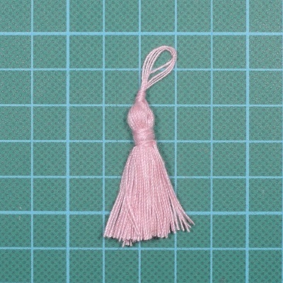 Pendente de fio rosa claro com franja sobre superfície quadriculada verde