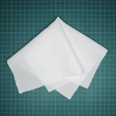 Pano de microfibra branco com bordas recortadas sobre superfície quadriculada verde.