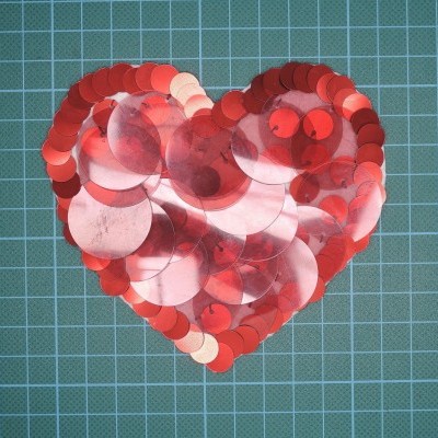 Coração de lantejoulas vermelhas e prateadas sobre fundo verde quadriculado