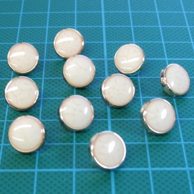 Doze botões redondos creme com base metálica em fundo verde quadriculado