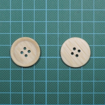 Dois botões de madeira clara com quatro furos sobre superfície verde com grade branca.