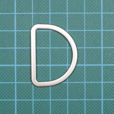 Argola metálica em formato de D sobre superfície de corte verde com grade azul