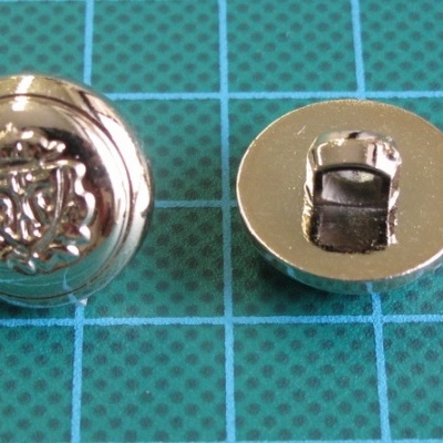 Dois botões metálicos prateados com brasão em relevo sobre superfície de corte verde