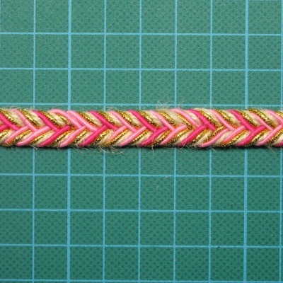 Fita decorativa trançada em rosa, dourado e branco numa mesa verde quadriculada
