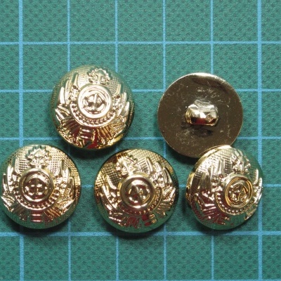 Cinco botões dourados ornamentais em superfície verde quadriculada.