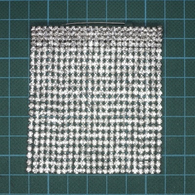 Manta prateada de pedras brilhantes em padrão quadrado sobre superfície de grade verde