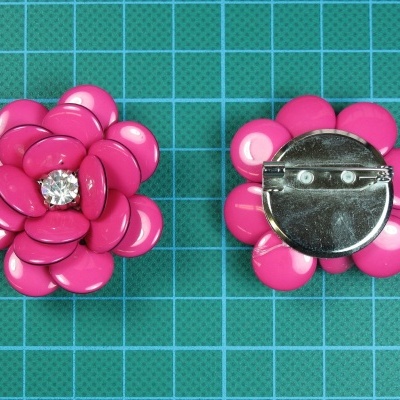 Botões de flor rosa com pedra e fecho prateado sobre base quadriculada verde