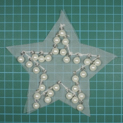 Estrela decorativa de rede com pérolas e fio prateado sobre superfície quadriculada verde