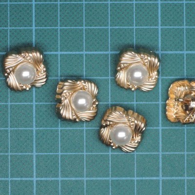 Cinco botões dourados quadrados com pérolas falsas no centro sobre superfície quadriculada azul