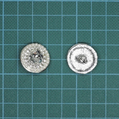 Par de botões prateados com pedrinhas sobre tapete de corte verde