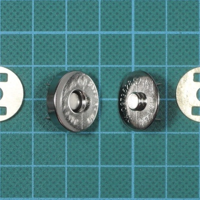 Botões de pressão metálicos e partes brancas com recortes em fundo quadriculado azul