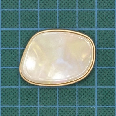 Broche dourado com madrepérola sobre tabuleiro verde quadriculado