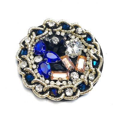 Broche redondo com pedras azuis, transparentes e rosadas em fundo preto