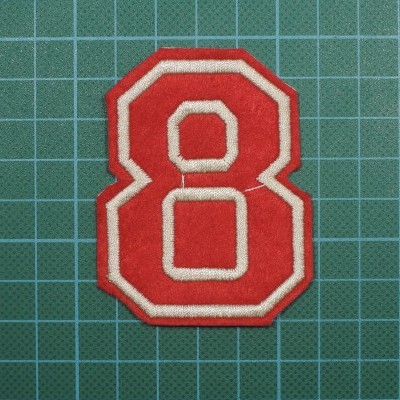 Patch têxtil número 8 vermelho com contorno branco sobre base verde quadriculada