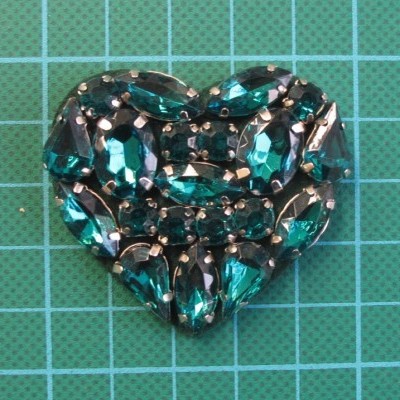 Broche coração com cristais verdes em superfície verde quadriculada