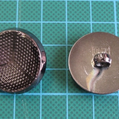 Dois botões metálicos redondos, um texturizado e outro com gancho para costura, sobre fundo azul com grade.