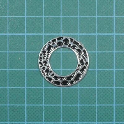 Anel circular em metal prateado com padrão em relevo sobre fundo verde quadriculado