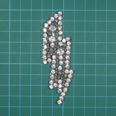 Broche em forma de raio com pedras brilhantes sobre fundo verde quadriculado