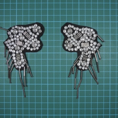 Aplicações em tecido preto com pedraria prateada e espaçadores metálicos sobre superfície de corte verde