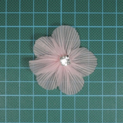 Flor decorativa de tecido rosa claro com ornamento central brilhante sobre grelha azul