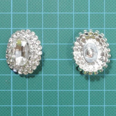 Par de brincos ovais com pedras transparentes e cristais em volta sobre superfície verde quadriculada