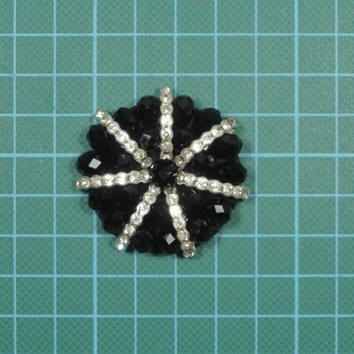 Broche redondo preto com cristais transparentes em fundo azul quadriculado