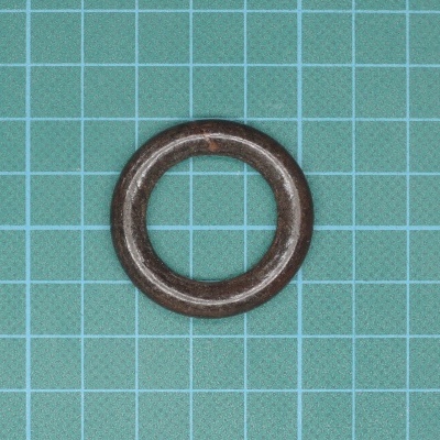 Anel metálico oxidado castanho sobre superfície verde quadriculada