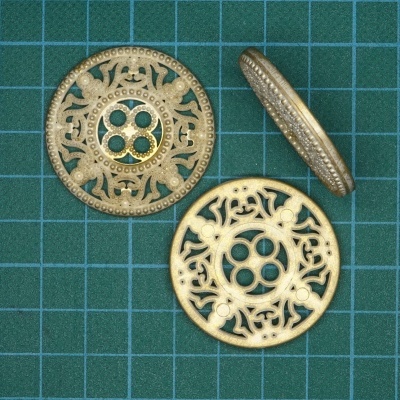 Três botões dourados com padrão ornamental em superfície verde quadriculada