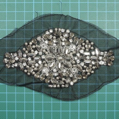 Peça com pedras decorativas em tecido preto sobre superfície gradeada verde