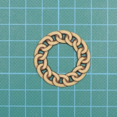 Anel em madeira com padrão de elos entrelaçados sobre superfície azul quadriculada