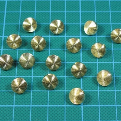 Botões metálicos dourados com padrão circular sobre base verde quadriculada