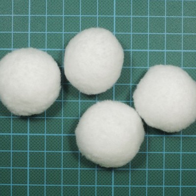 Quatro bolas brancas de algodão sobre superfície verde quadriculada.