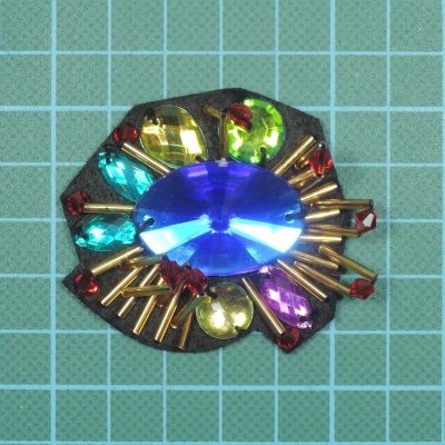 Broche decorativo colorido em base escura sobre superfície quadriculada verde