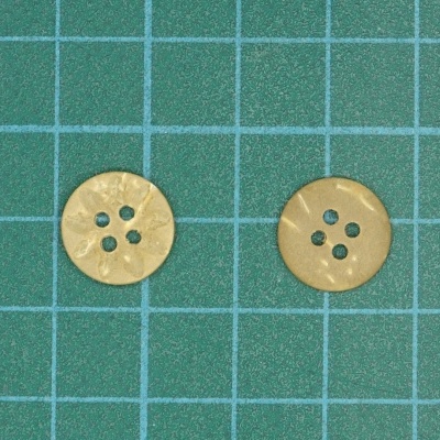 Dois botões dourados redondos com quatro furos sobre fundo verde com grade azul