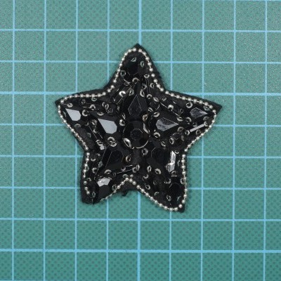 Aplicação estrela preta com pedras e contas sobre fundo quadriculado azul.