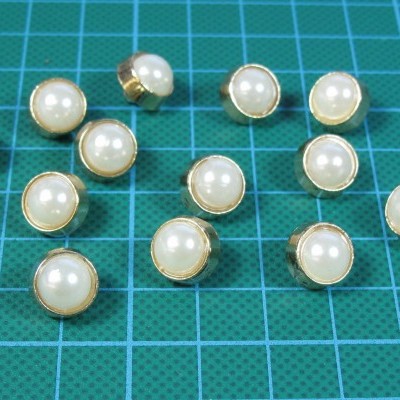 Botões redondos dourados com pérola branca em fundo verde quadriculado