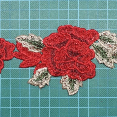 Aplicação bordada floral em tecido com flores vermelhas e folhas verdes, sobre fundo quadriculado verde