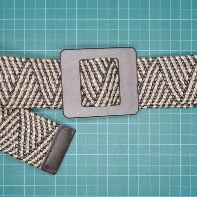 Cinto tecido bege e preto com fivela quadrada preta sobre superfície verde com grade