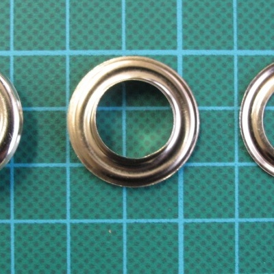 Ilhós metálicos prateados de vários tamanhos sobre superfície quadriculada verde