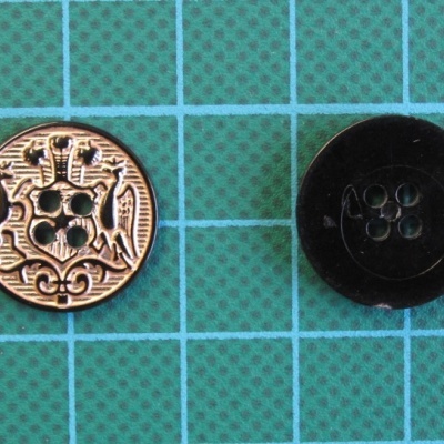 Dois botões redondos, um dourado com padrão de dragão e outro preto liso, sobre fundo verde com grade azul.